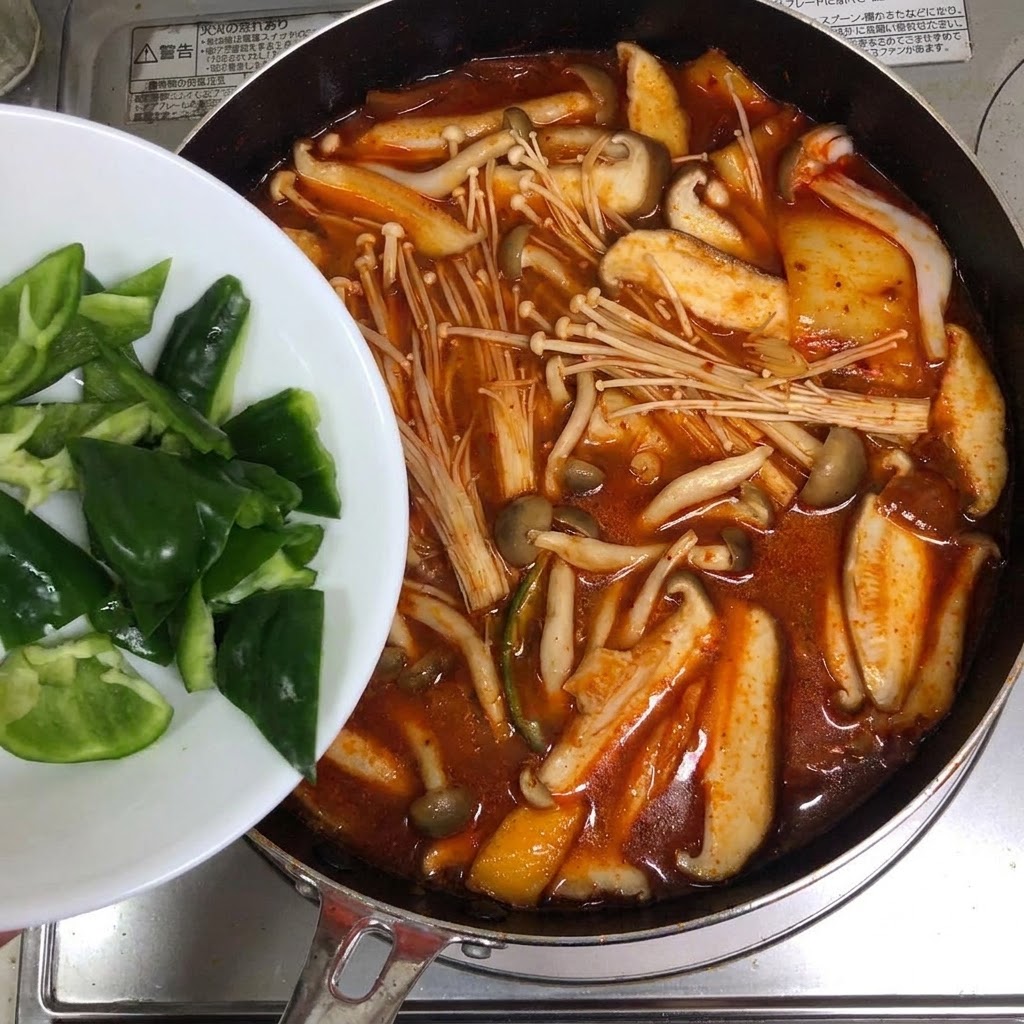 Tranches de piments verts ajoutées dune assiette blanche dans une casserole de soupe au kimchi rouge.