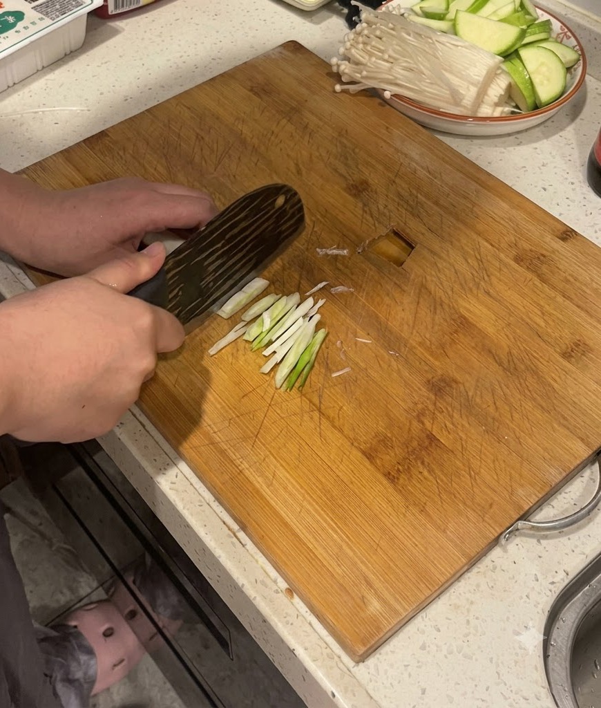 Mains utilisant un couteau de cuisine pour trancher des tiges doignon vert sur une planche à découper en bois.
