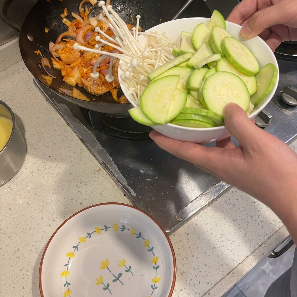 Courgettes tranchées et champignons enoki versés dun bol dans un wok contenant du porc et des oignons sautés.