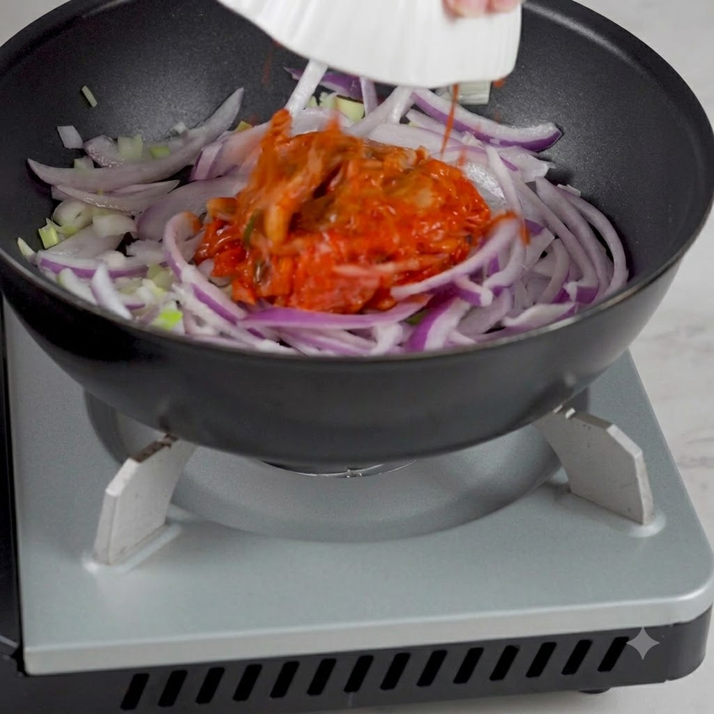 Du kimchi coréen ajouté dun bol dans la poêle contenant les oignons sautés.