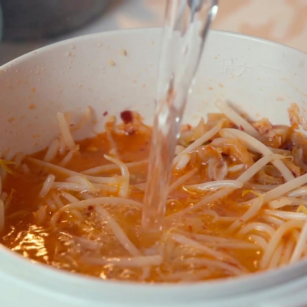 De leau versée par le dessus dans la casserole contenant le kimchi et les pousses de soja.