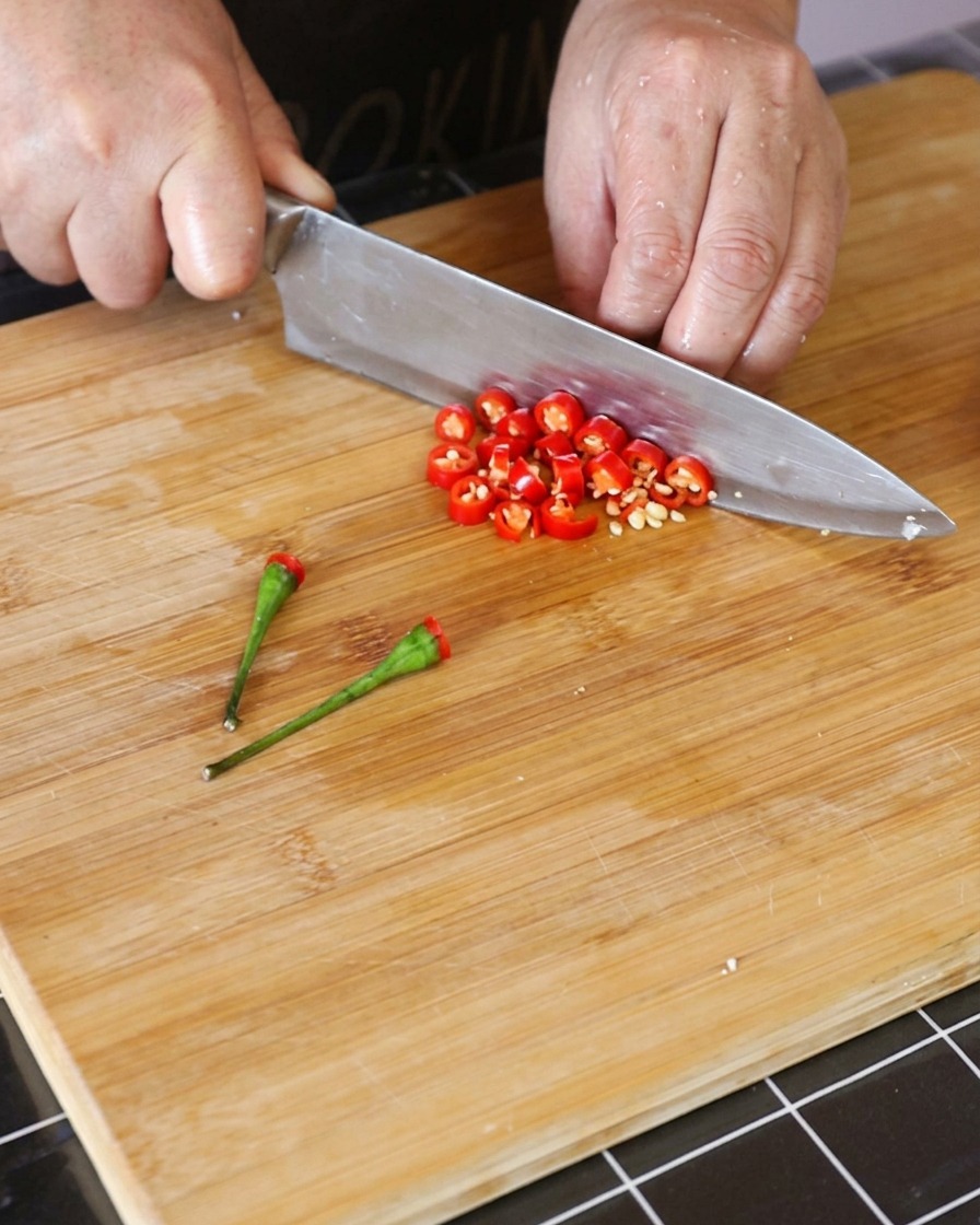 Piments rouges thaï frais coupés en petits anneaux sur une planche à découper en bois.