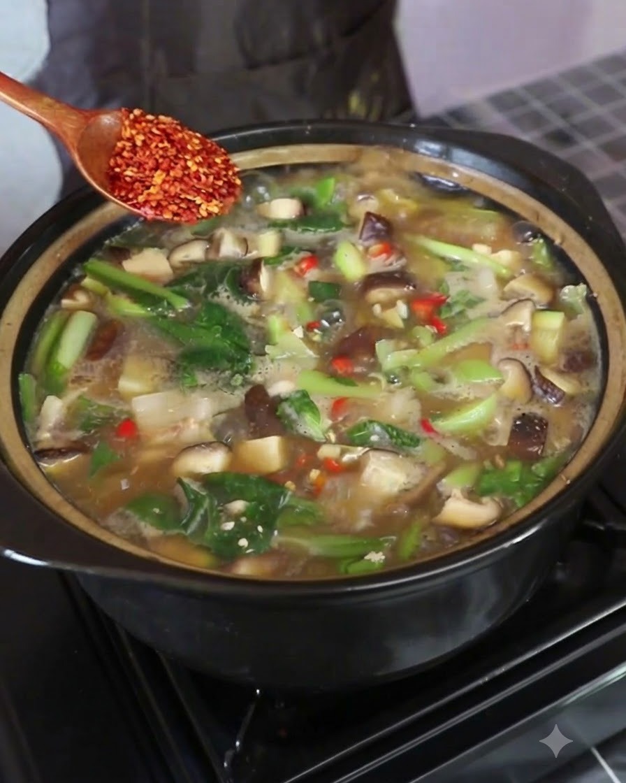 Une cuillère en bois tenant des flocons de chili rouge au-dessus de la casserole de soupe bouillante.