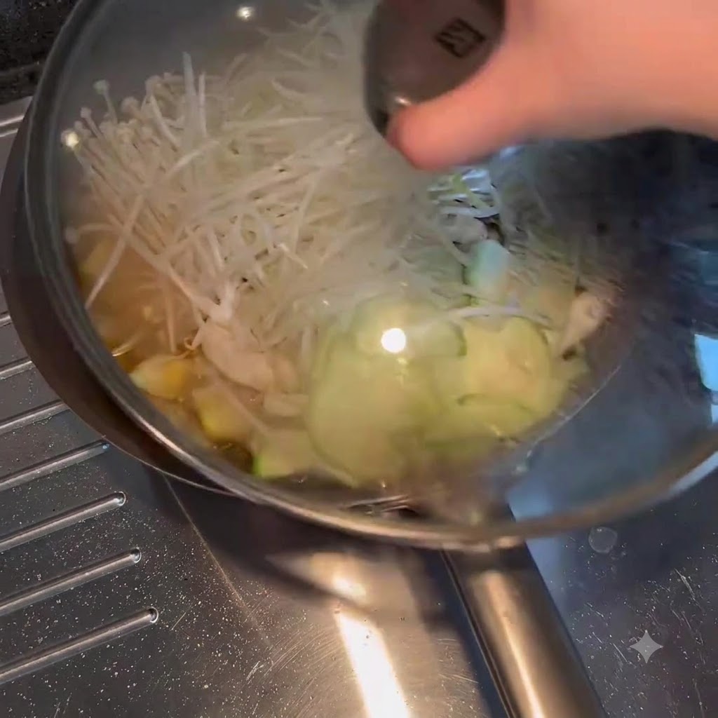 Un couvercle en verre placé sur une poêle remplie de légumes et de bouillon frémissants.