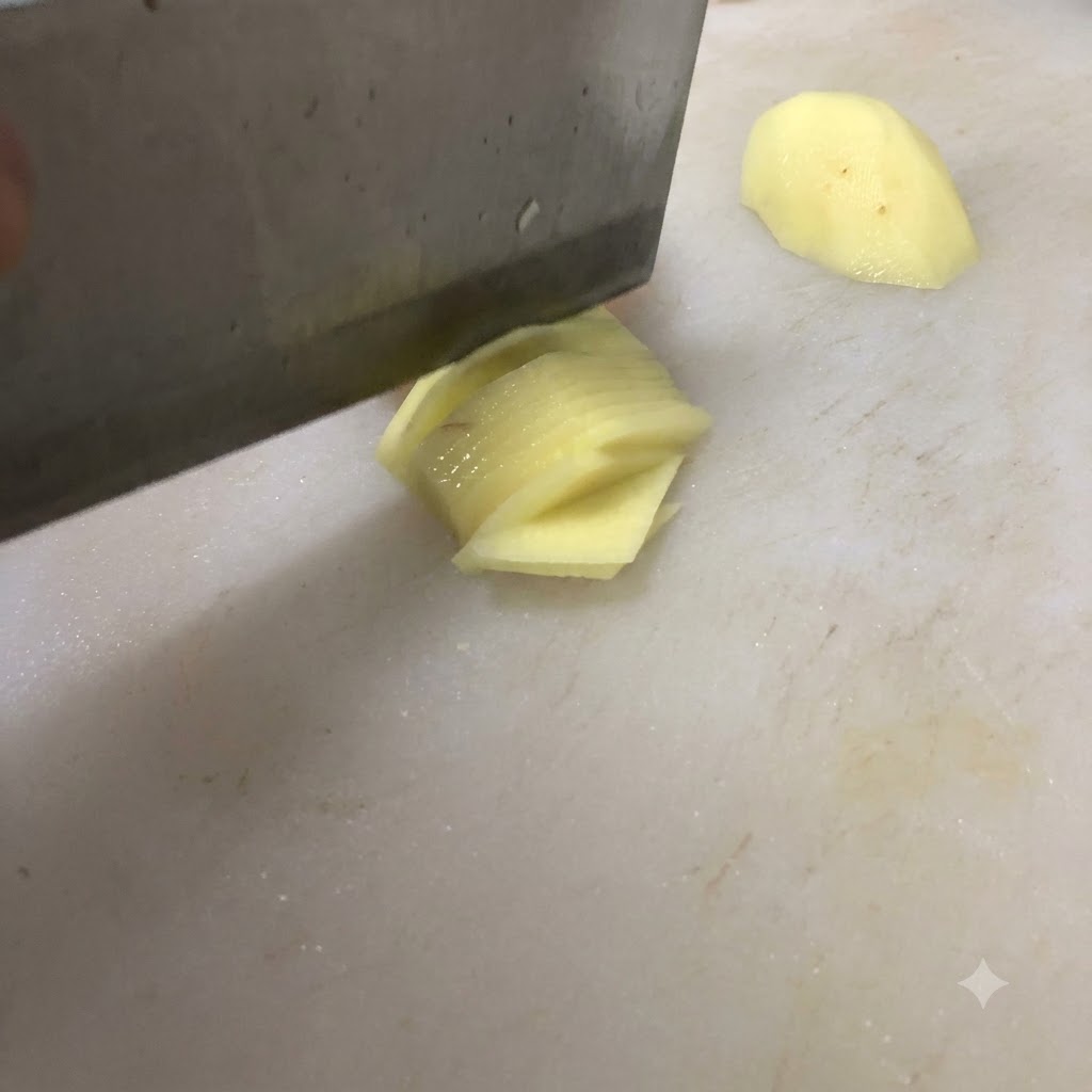 Un couteau coupant une pomme de terre en fines tranches sur une planche à découper blanche.