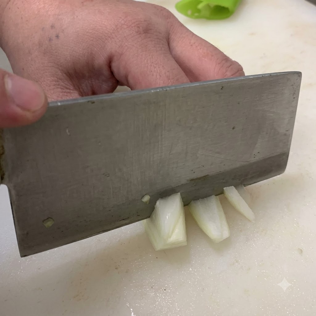 Un couteau coupant un oignon en morceaux sur une planche à découper blanche.
