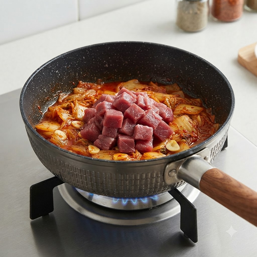 Cubes de bœuf crus disposés sur le kimchi sauté dans une casserole.