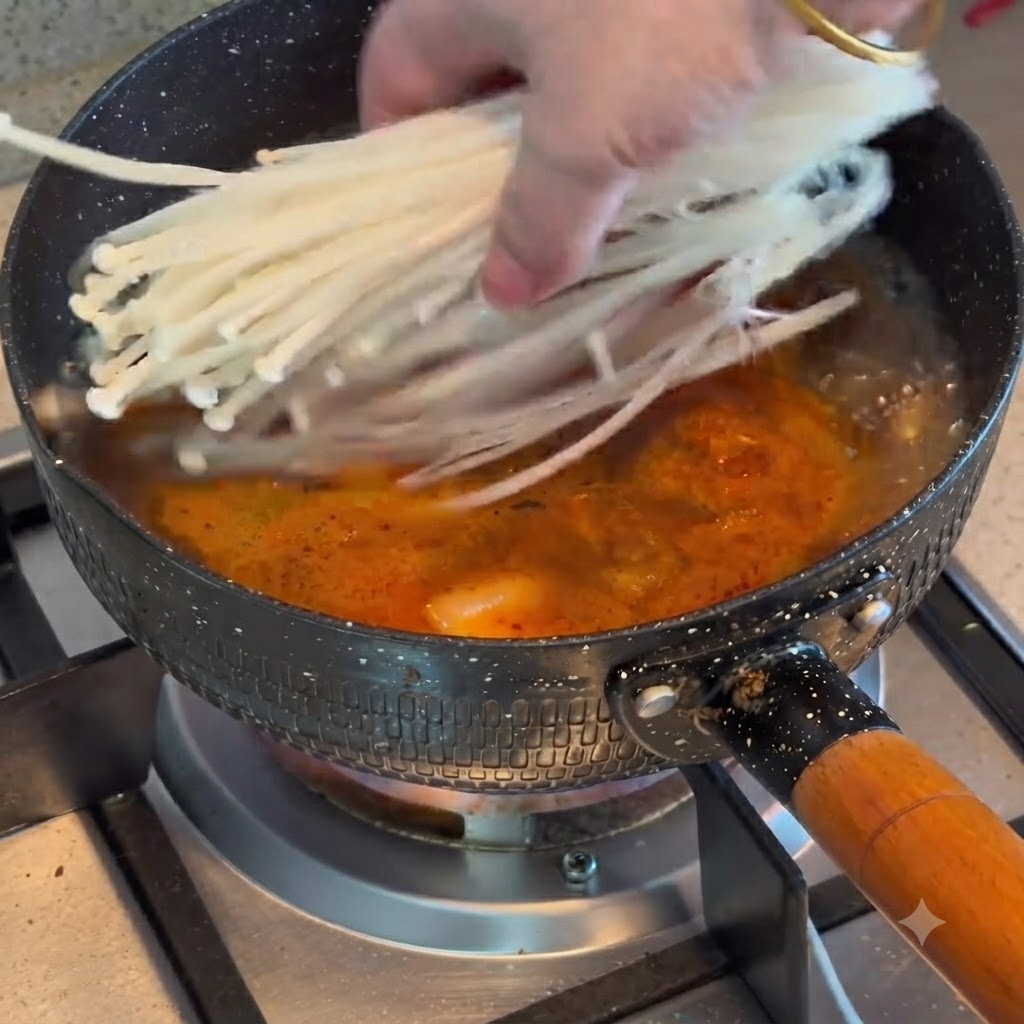 Champignons enoki ajoutés dans une casserole de ragoût de kimchi et de bœuf bouillant.