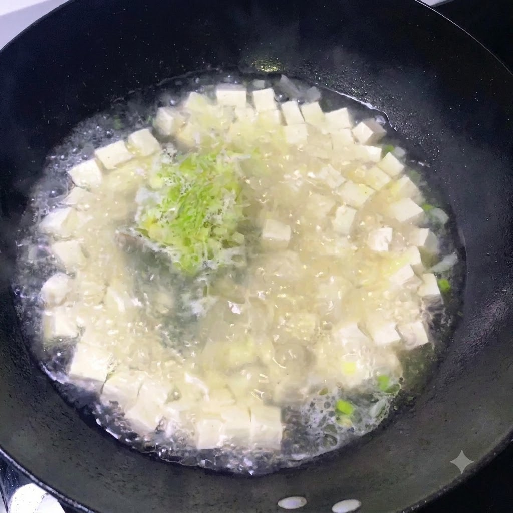 Des assaisonnements saupoudrés sur une marmite frémissante de tofu et doignons verts hachés.