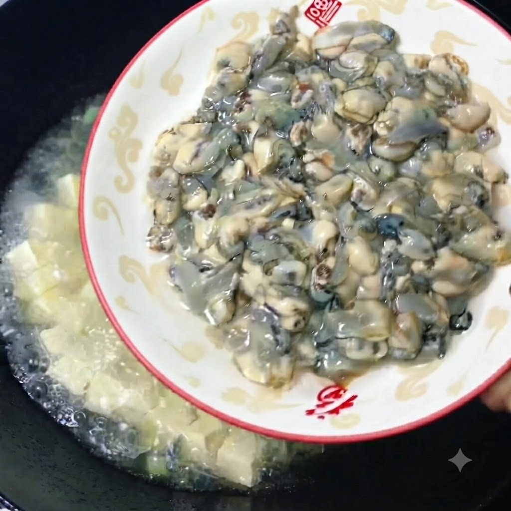 Des huîtres crues charnues et fraîches glissant dune assiette décorative dans un wok de bouillon de tofu frémissant.