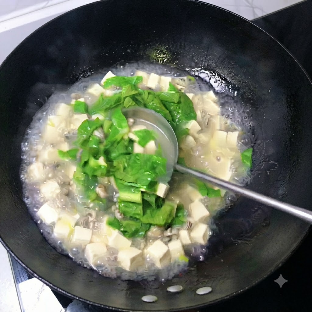 Une louche remuant un bouillon laiteux rempli de cubes de tofu, dhuîtres et de feuilles vertes dans un wok.