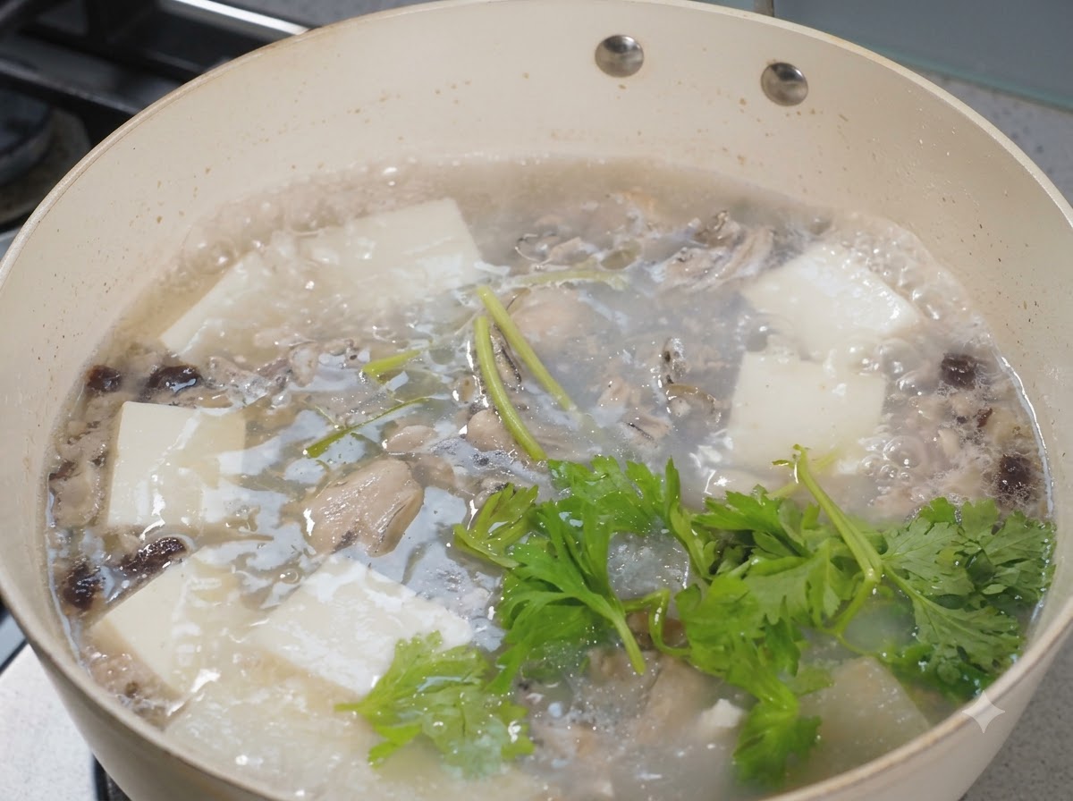 Des feuilles de céleri fraîches dispersées sur une casserole bouillante de soupe aux huîtres et au tofu.