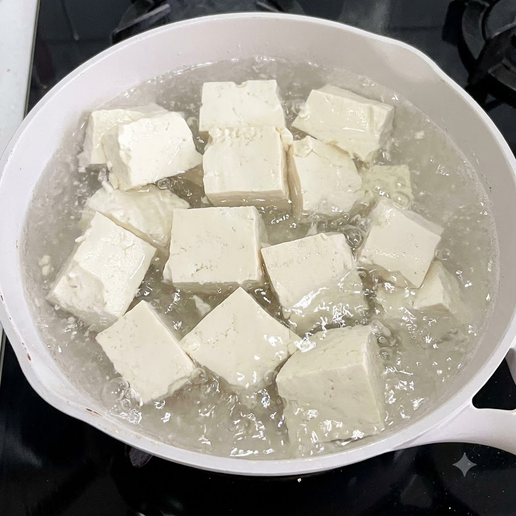 Des cubes de tofu bouillant dans une casserole deau blanche avec des tranches de gingembre.