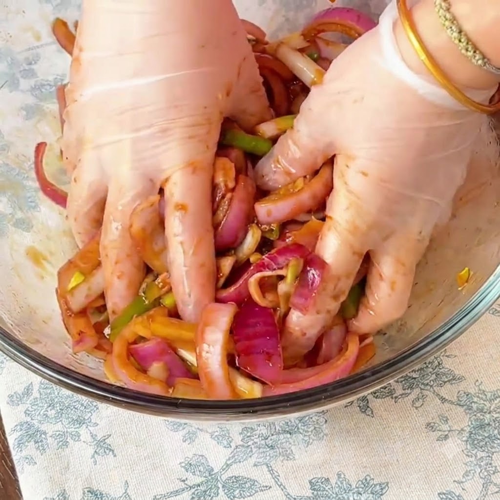 Mains gantées massant soigneusement la marinade et les oignons rouges dans le poulet à lintérieur dun bol en verre.