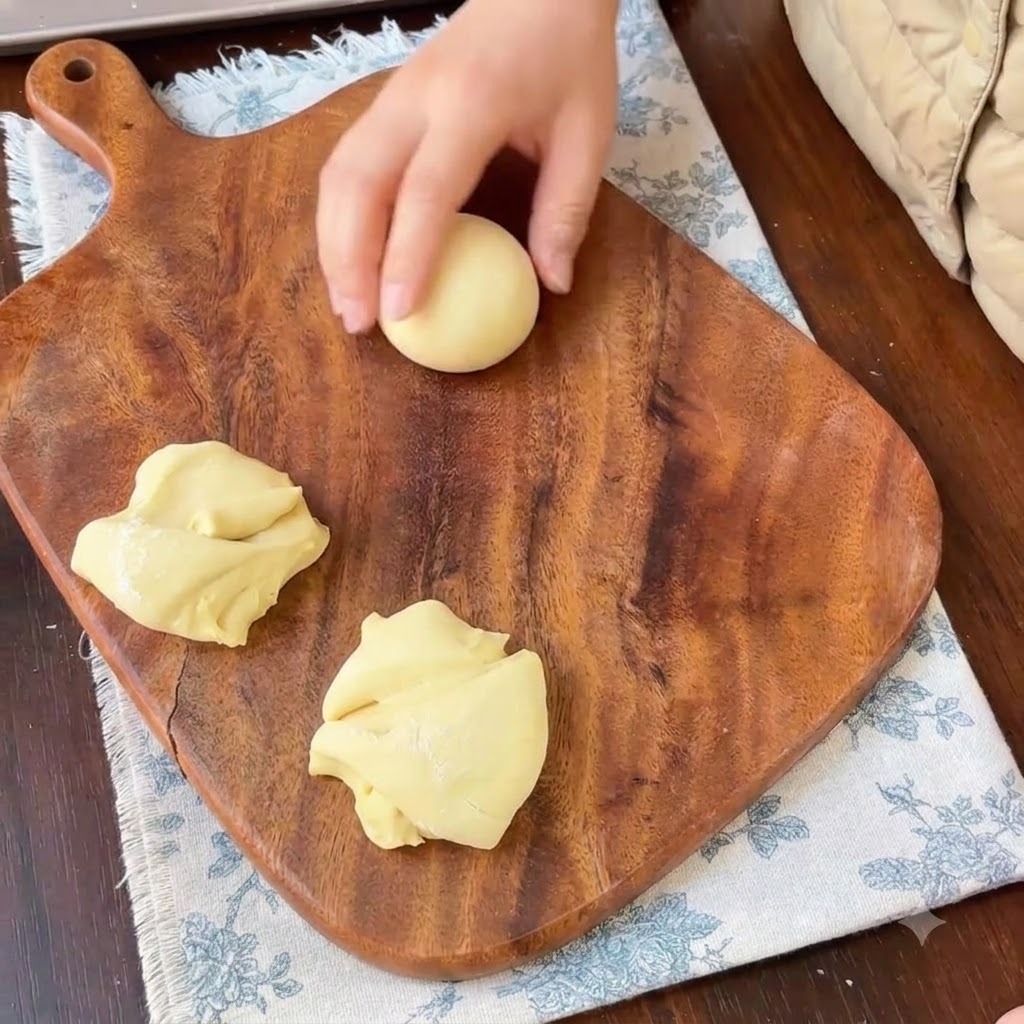 Une main roulant un morceau de pâte jaune en une boule sphérique bien lisse.