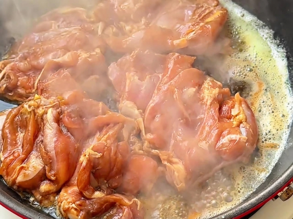 Morceaux de poulet marinés crépitant dans une poêle chaude avec du beurre fondu.