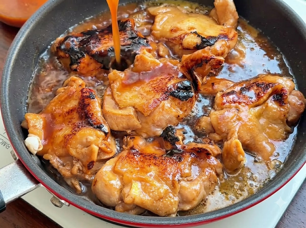 Un filet de sauce brune versé sur les hauts de cuisse de poulet dorés dans la poêle.