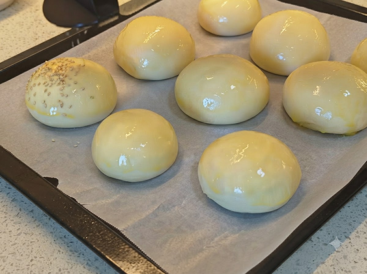 Graines de sésame en train dêtre saupoudrées sur une plaque de petits pains à pain brillants dorés à lœuf.