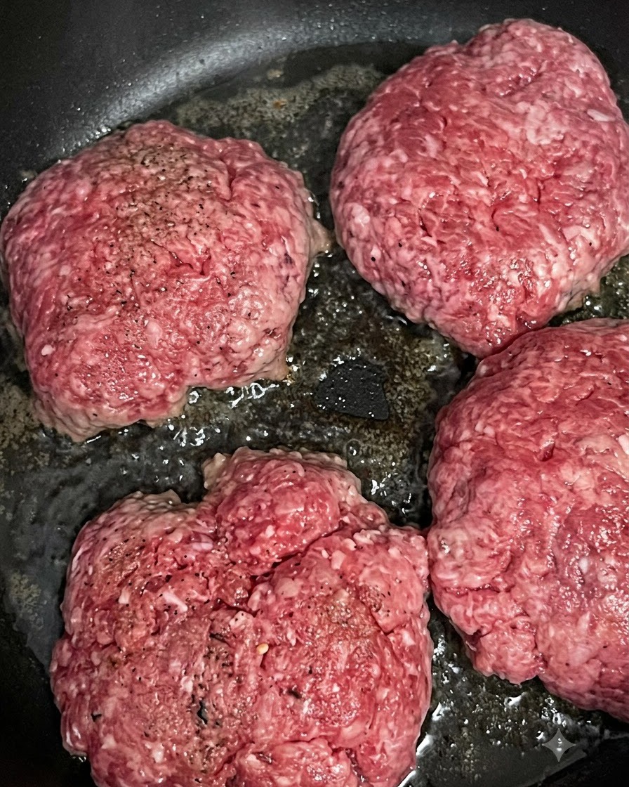 Quatre steaks de bœuf crus qui grésillent et dorent dans une poêle chaude.