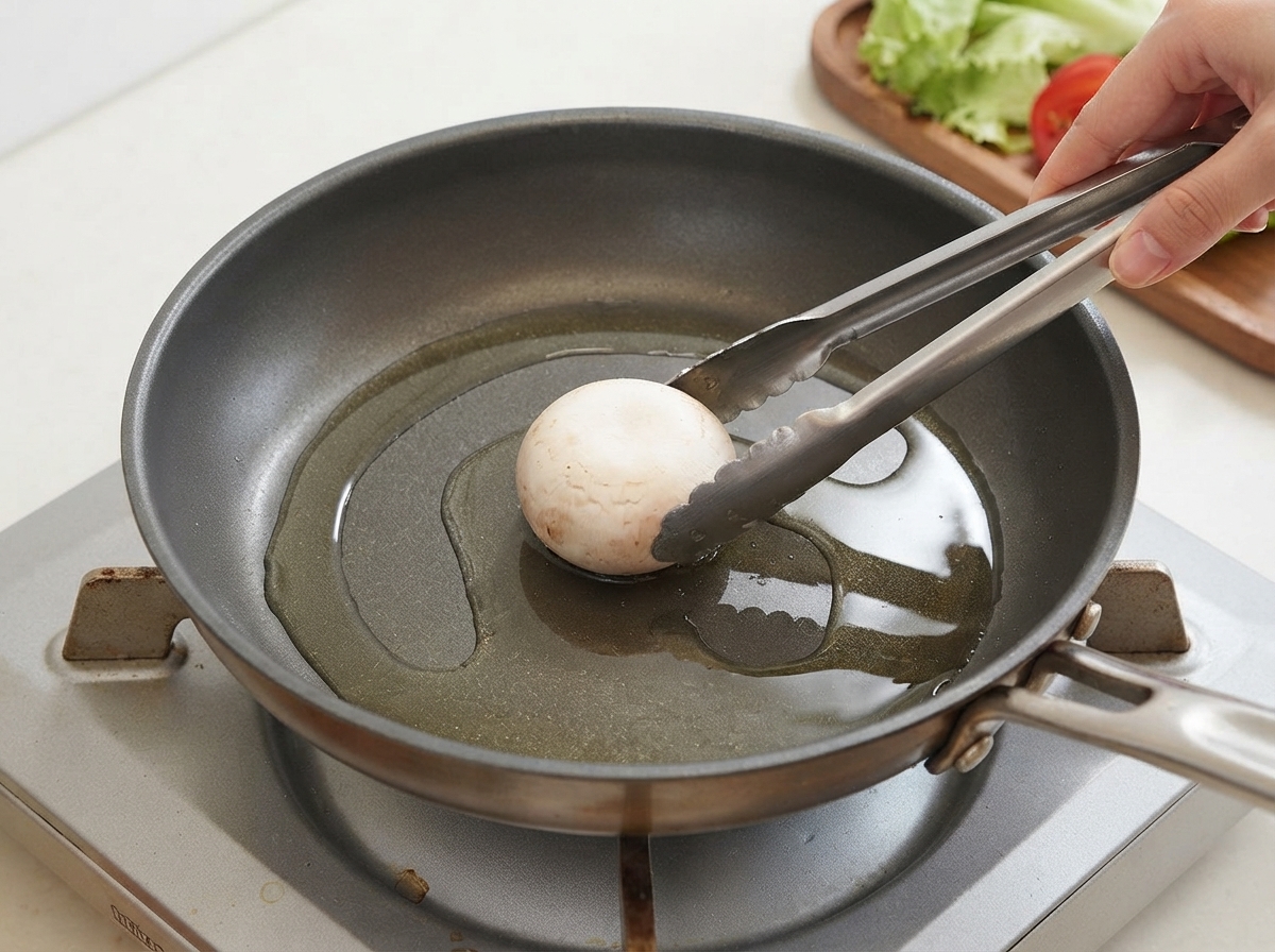 Un champignon placé à laide dune pince dans une poêle huilée.