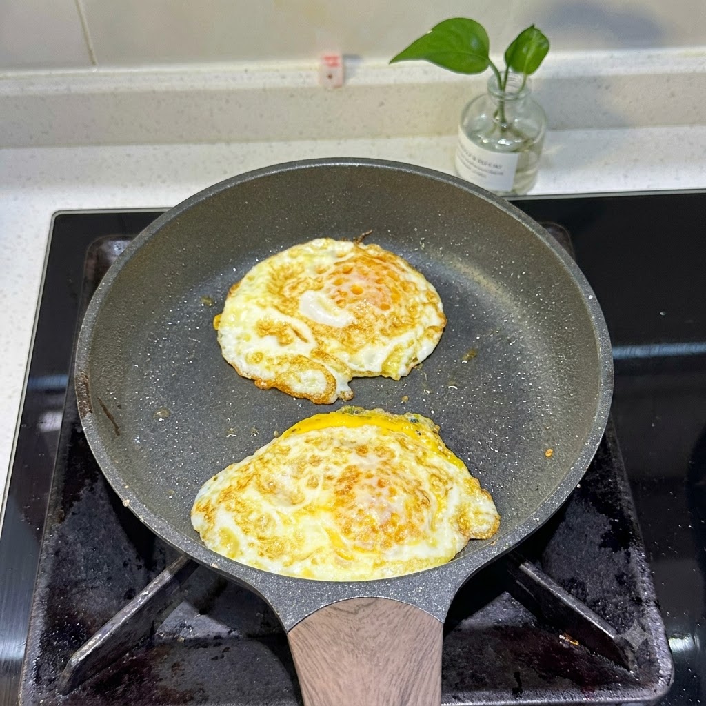 Deux œufs au plat cuisant dans une poêle avec des bords dorés.