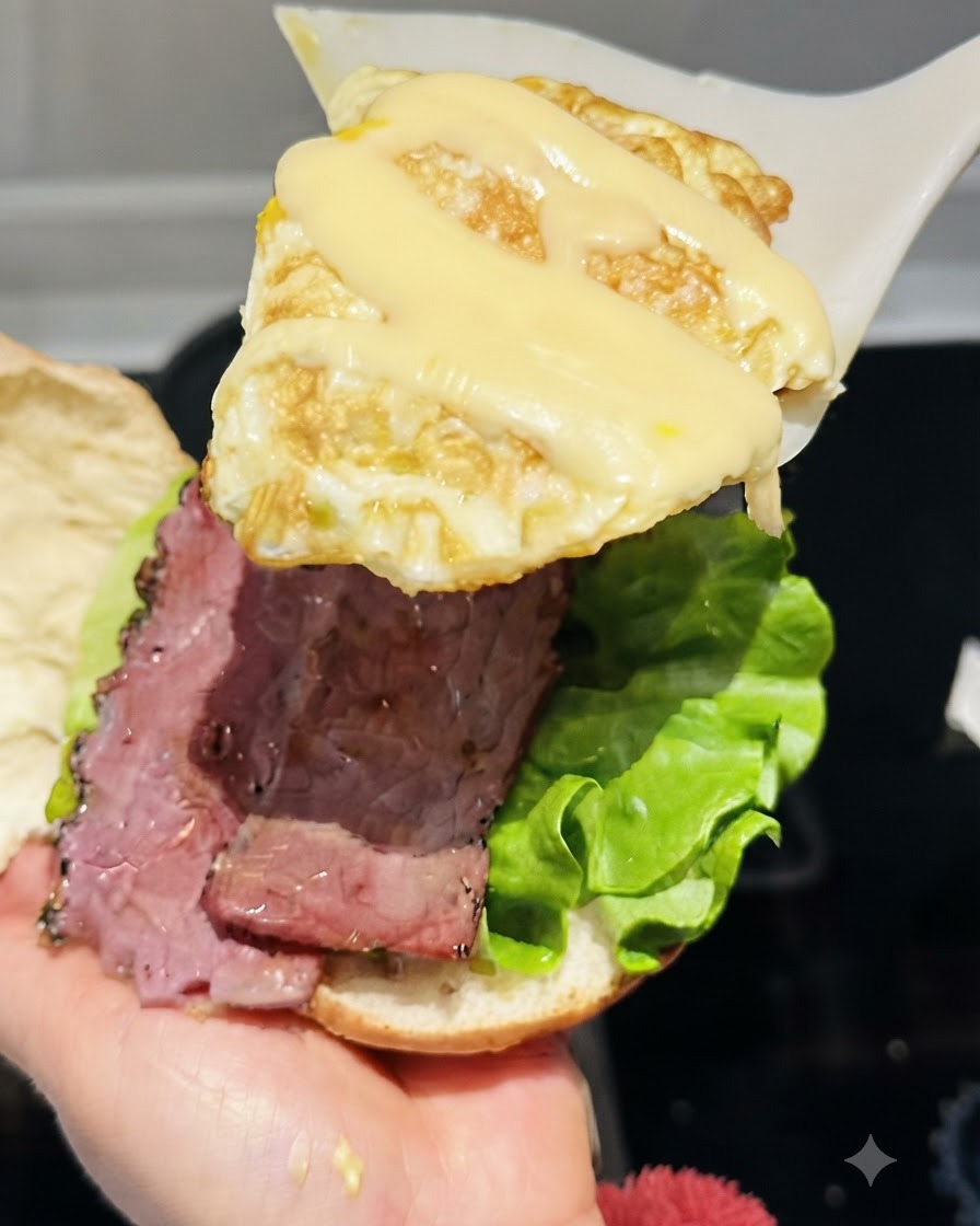 Une spatule soulevant un œuf au plat garni de fromage en ficelle fondu au-dessus de lassemblage du burger.