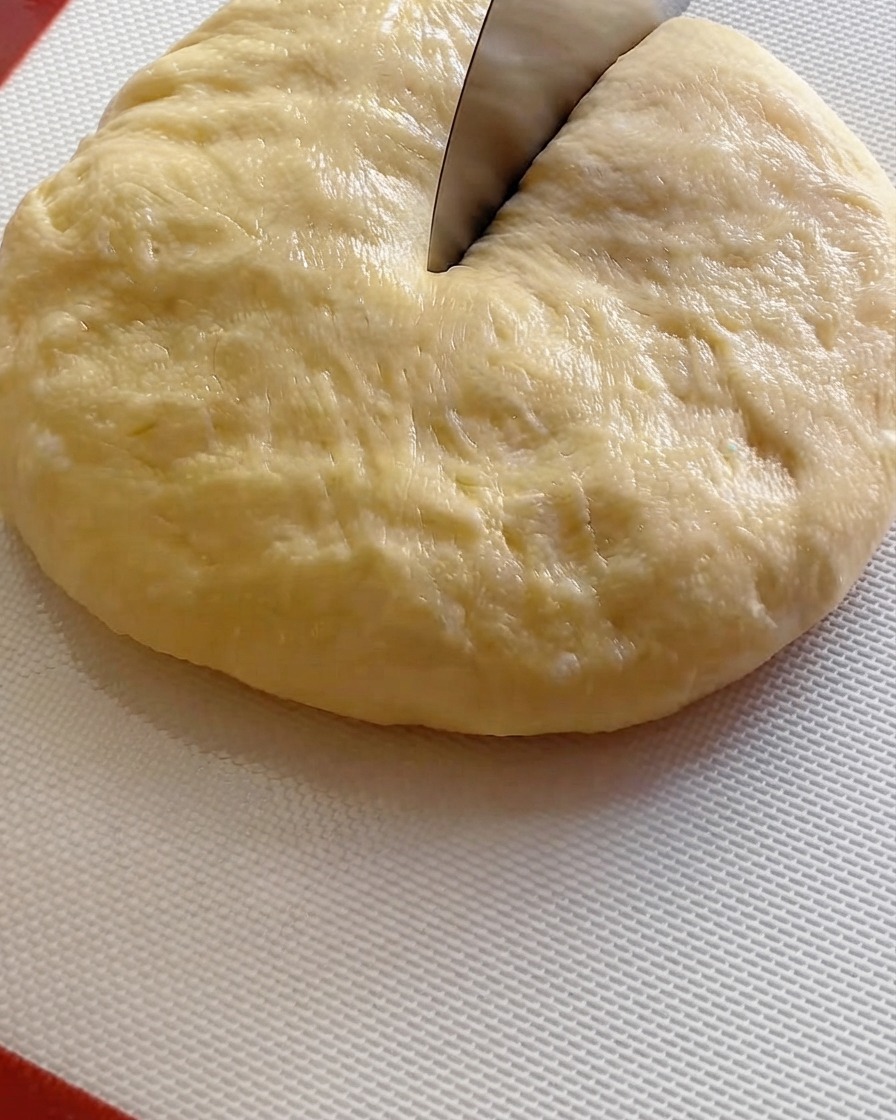 Corne à pâte coupant une grande boule de pâte fermentée en neuf portions égales sur un tapis blanc.