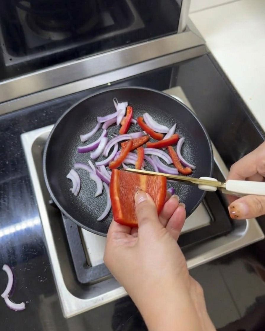 Oignons rouges et poivrons émincés dans une poêle assaisonnés de sel et de poivre avec des ciseaux de cuisine.