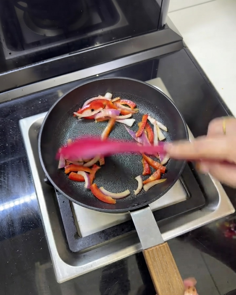 Morceaux de viande pré-cuits sautés avec des oignons rouges et des poivrons dans une poêle.