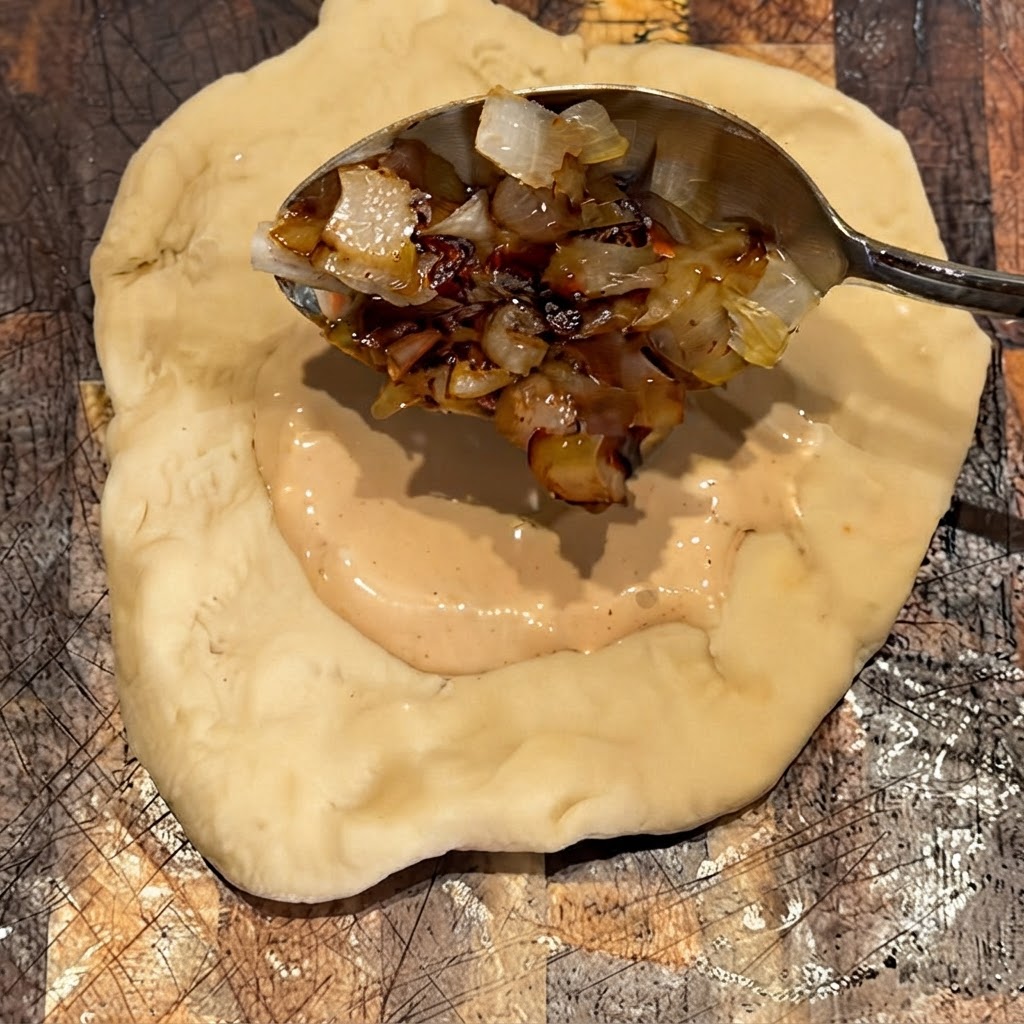 Des oignons grillés déposés à la cuillère sur la couche de sauce sur la pâte.