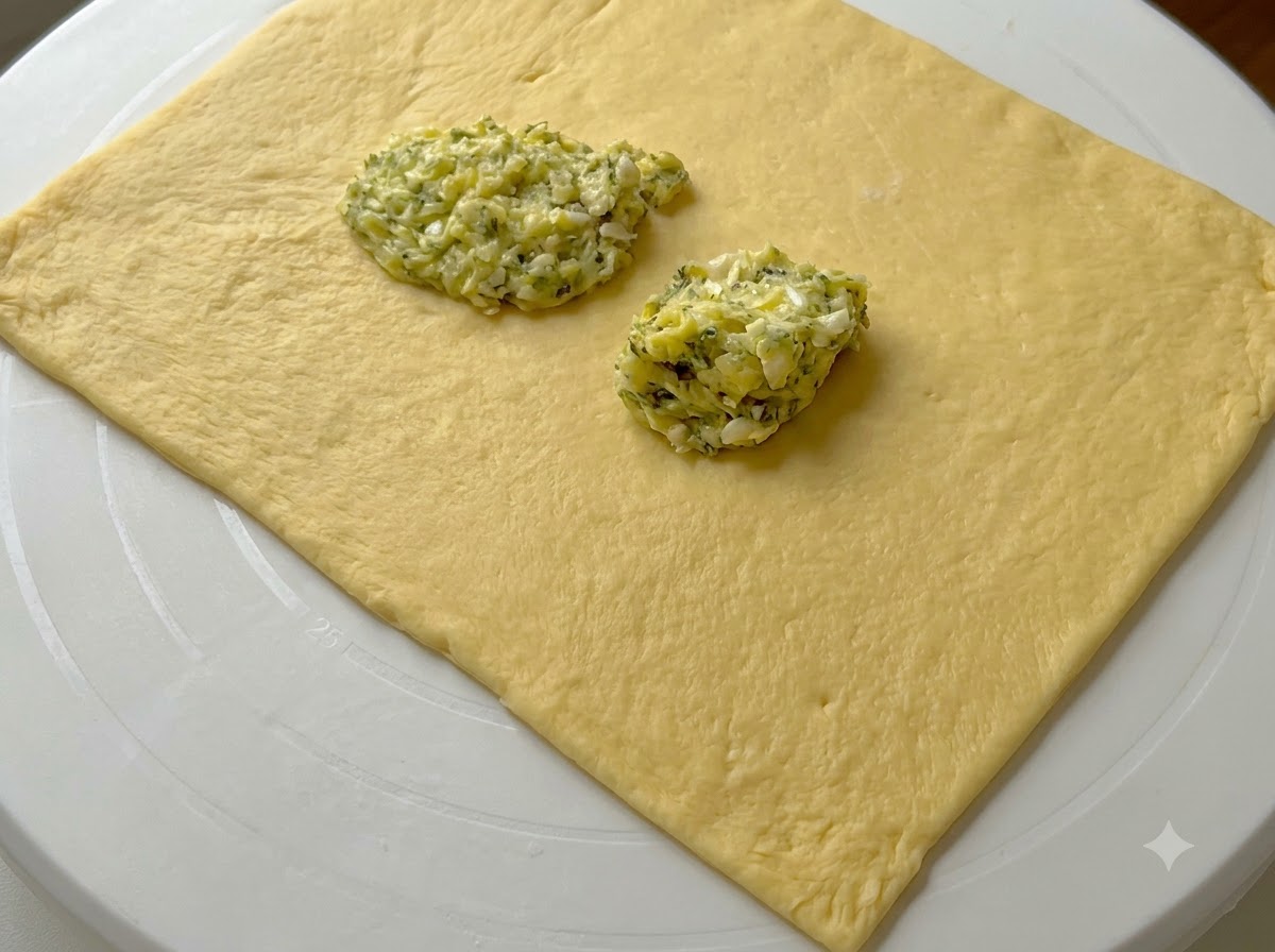 Des touches de préparation verte au beurre dail disposées sur une feuille de pâte rectangulaire abaissée.