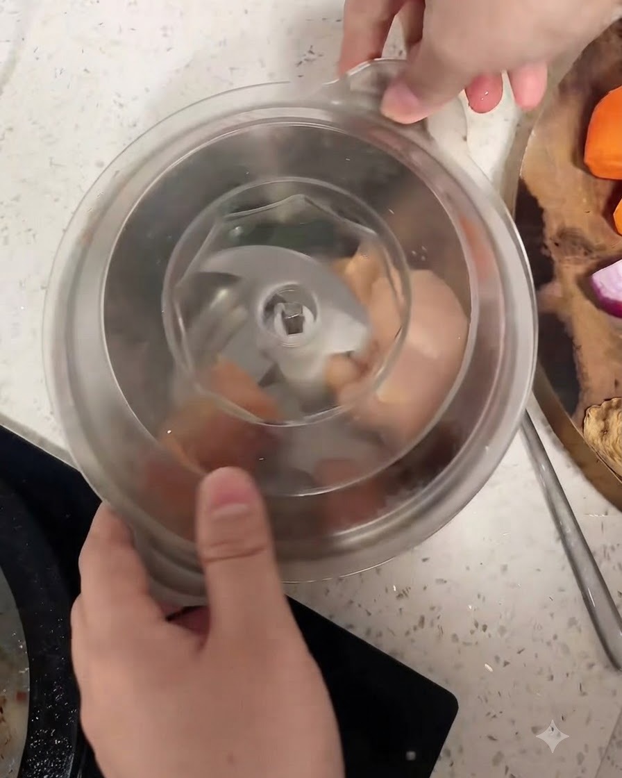 Morceaux de blanc de poulet cru à lintérieur du bol dun robot culinaire autour de la lame centrale.