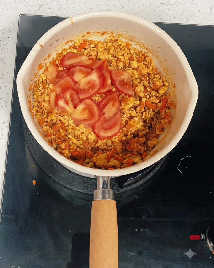 Tranches de tomates fraîches reposant sur le dessus du mélange de poulet et de légumes cuits dans une poêle.