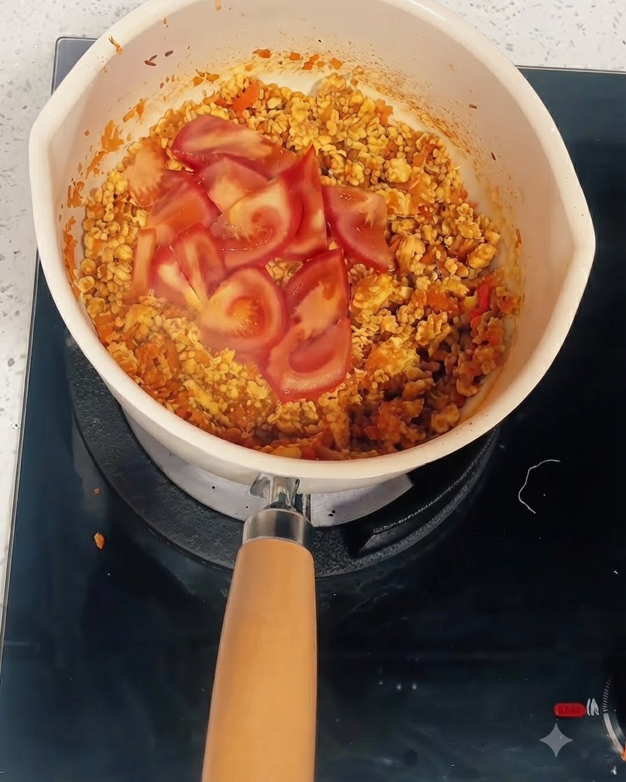Tranches de tomates sur le mélange cuit dans une casserole où leau et le concentré de tomate sont ajoutés.