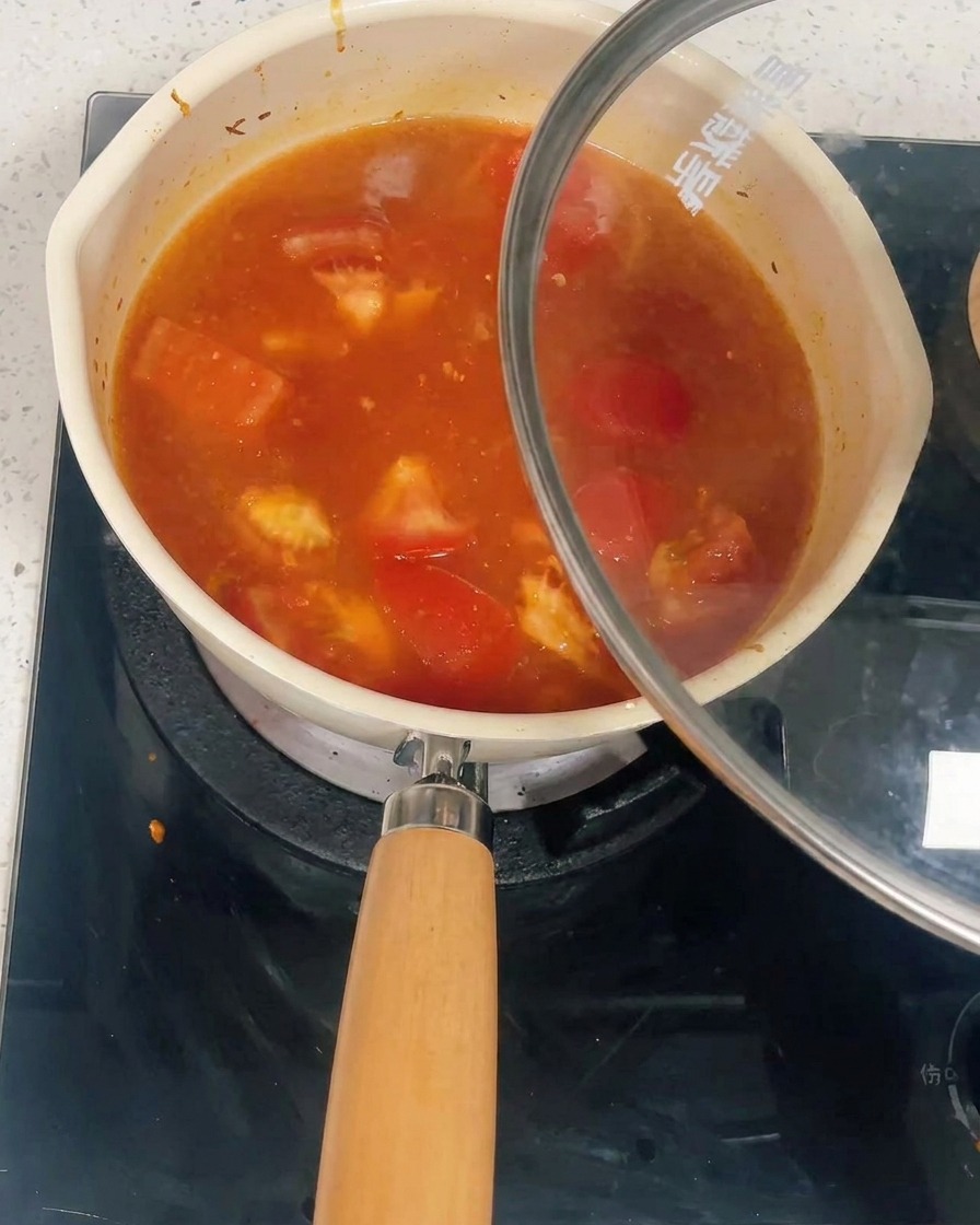 Une casserole remplie de sauce à la tomate et au poulet recouverte dun couvercle en verre.