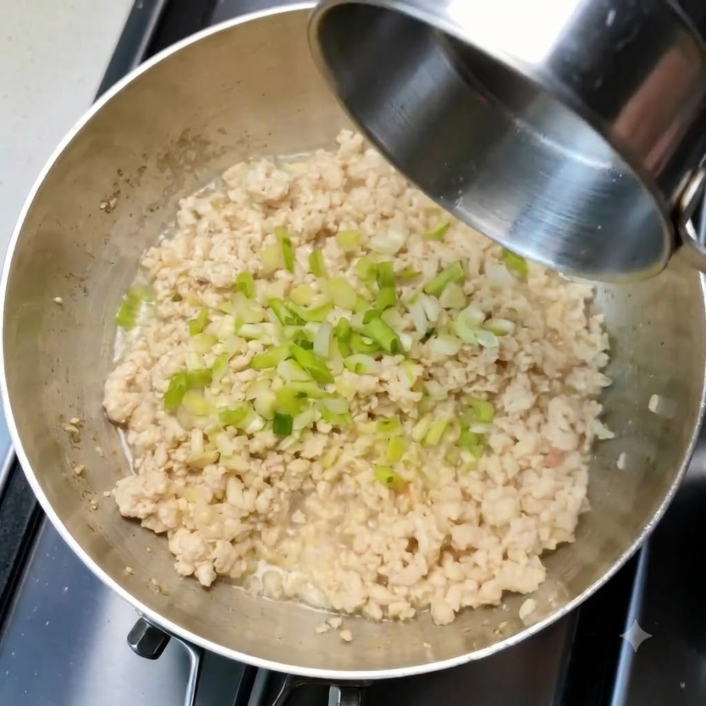 Des oignons verts hachés et de lail éparpillés sur le poulet haché cuit à lintérieur dune poêle.