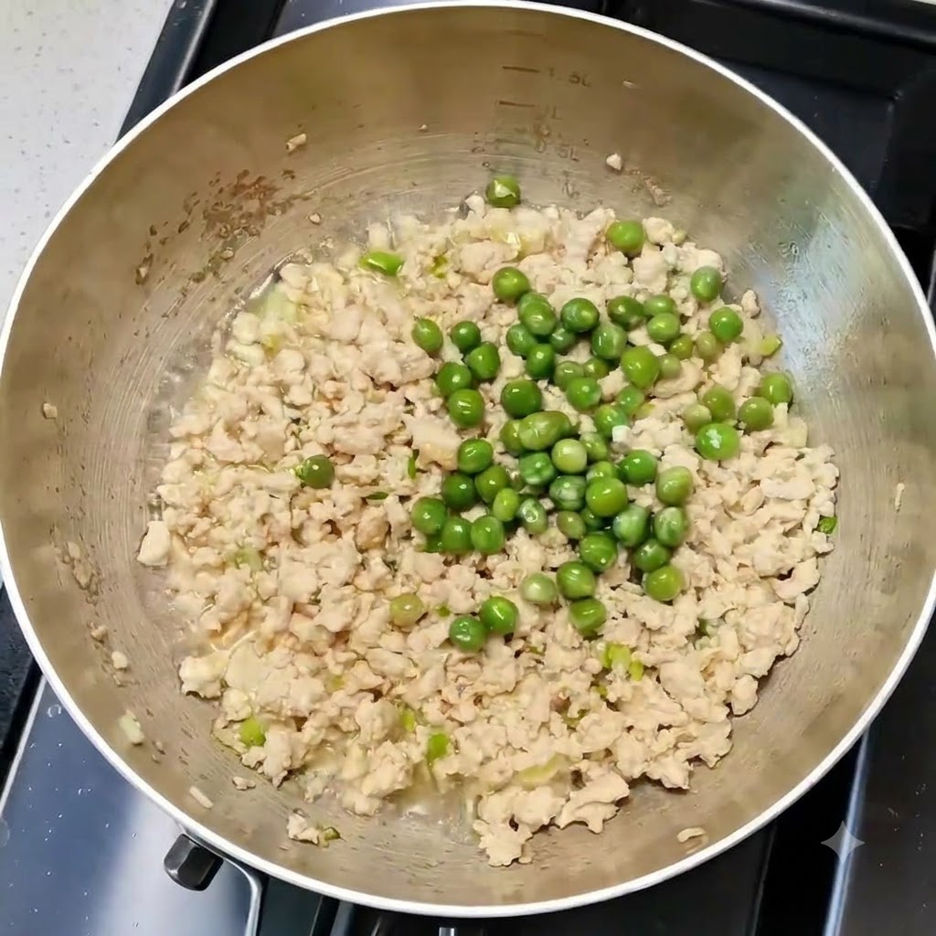 Des petits pois mélangés uniformément avec le poulet et les aromates dans une poêle de cuisson.