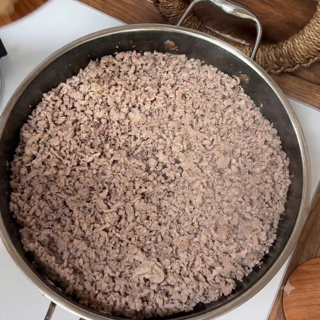 De la viande hachée cuite remplissant une poêle en acier inoxydable pendant la cuisson.