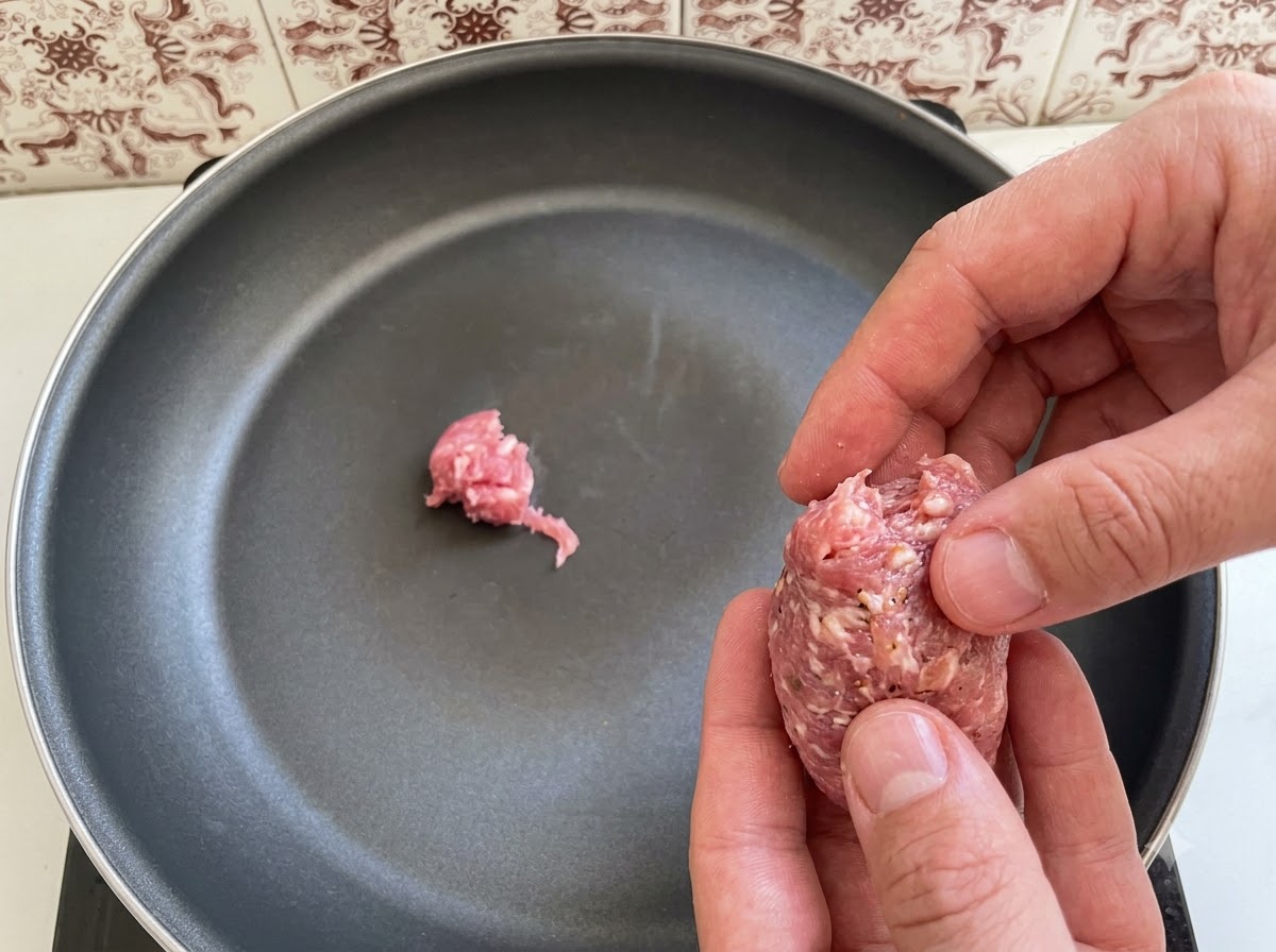 Des morceaux de chair à saucisse italienne disposés et placés dans une poêle.
