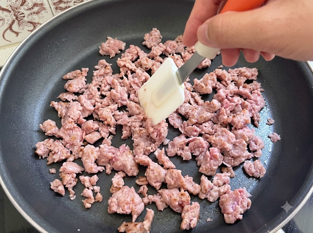 De la chair à saucisse italienne remuée et saisie activement à laide dune spatule dans une poêle.