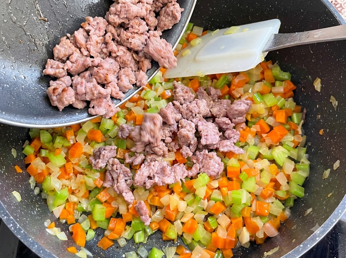 De la chair à saucisse cuite versée dune poêle dans la cocotte de légumes et mélangée.