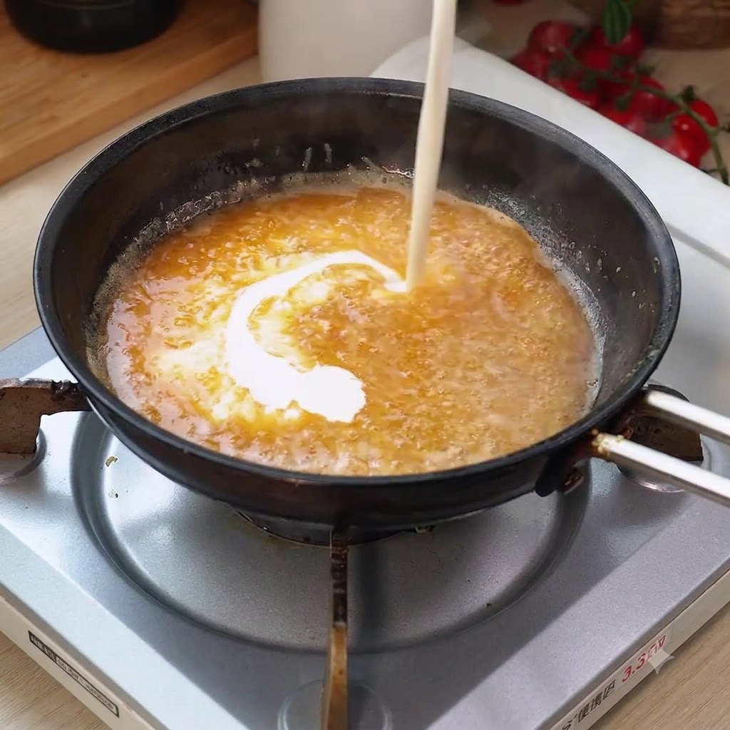 Crème fraîche versée dans la sauce bouillante de la poêle, créant un mélange tourbillonnant.