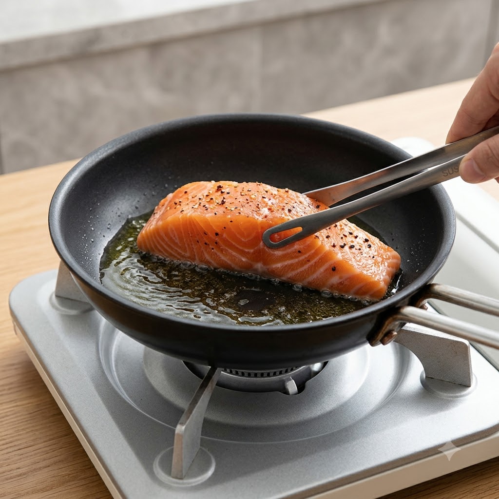 Filet de saumon frais placé côté peau vers le bas dans une poêle chaude huilée à laide de pinces.