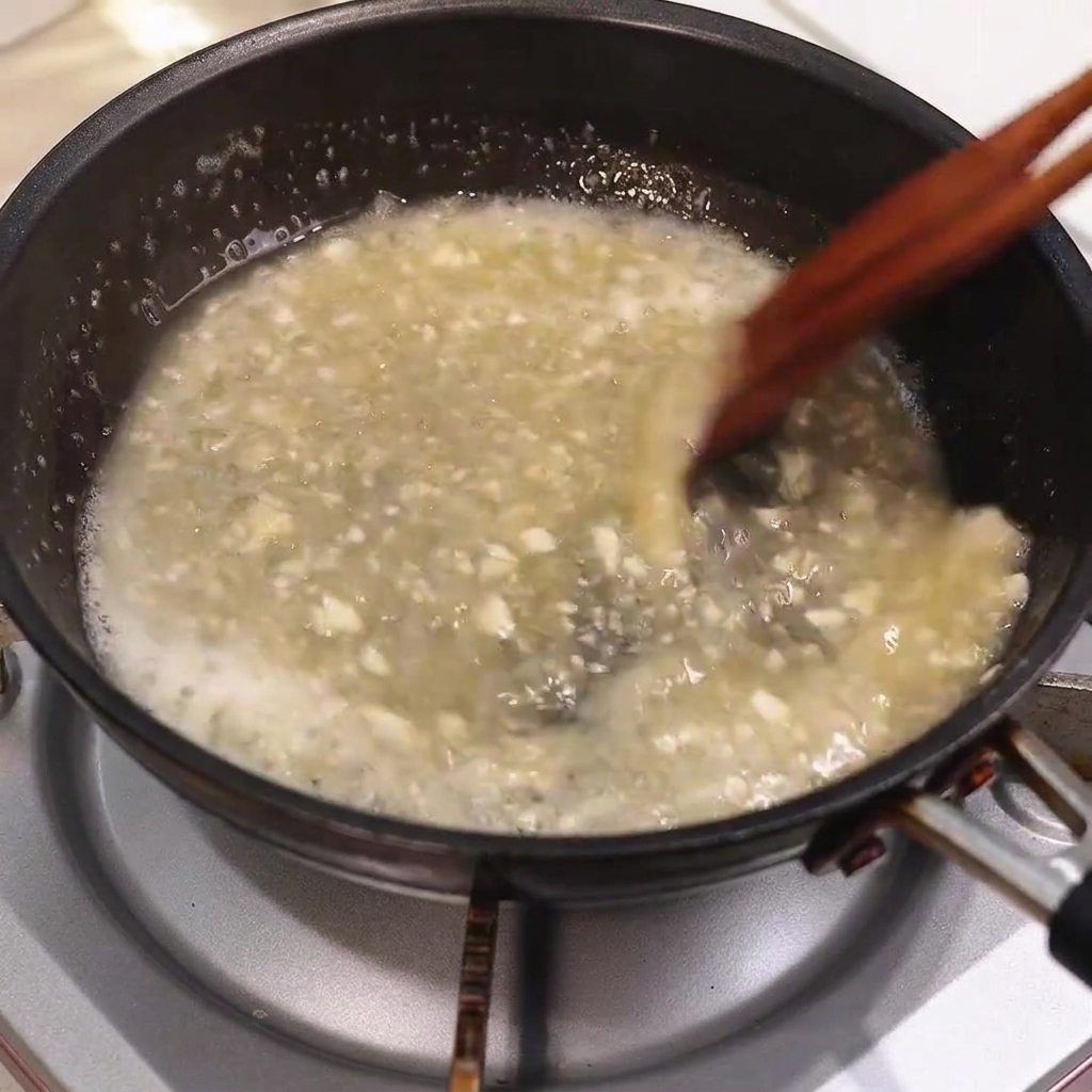 Beurre fondant dans une sauce de poêle bouillante tout en étant remué avec des baguettes en bois.