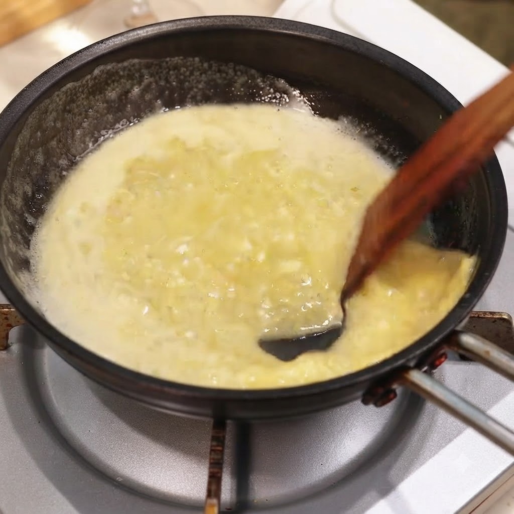 Poêle de sauce riche au beurre dail et citron mélangée à des herbes hachées avec une spatule en bois.