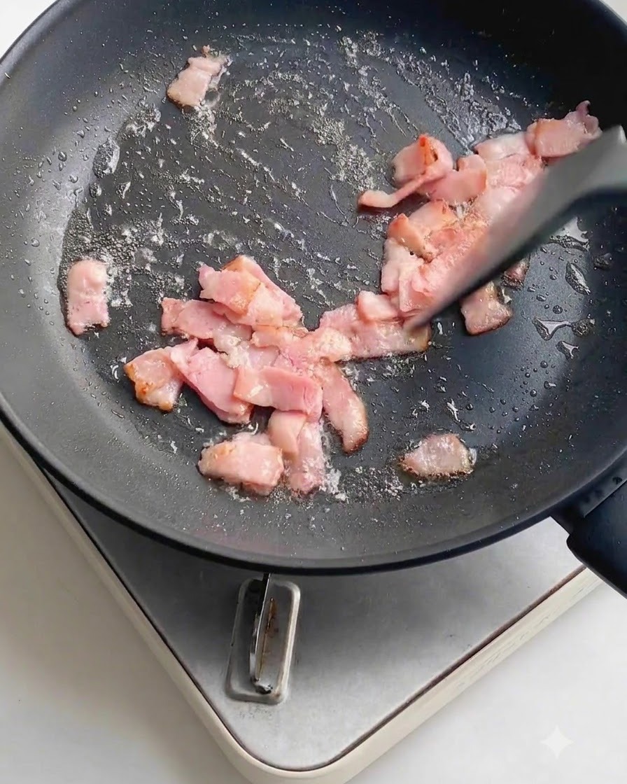 De lail frais émincé parsemé sur les morceaux de bacon en train de cuire à lintérieur dune poêle antiadhésive sombre.