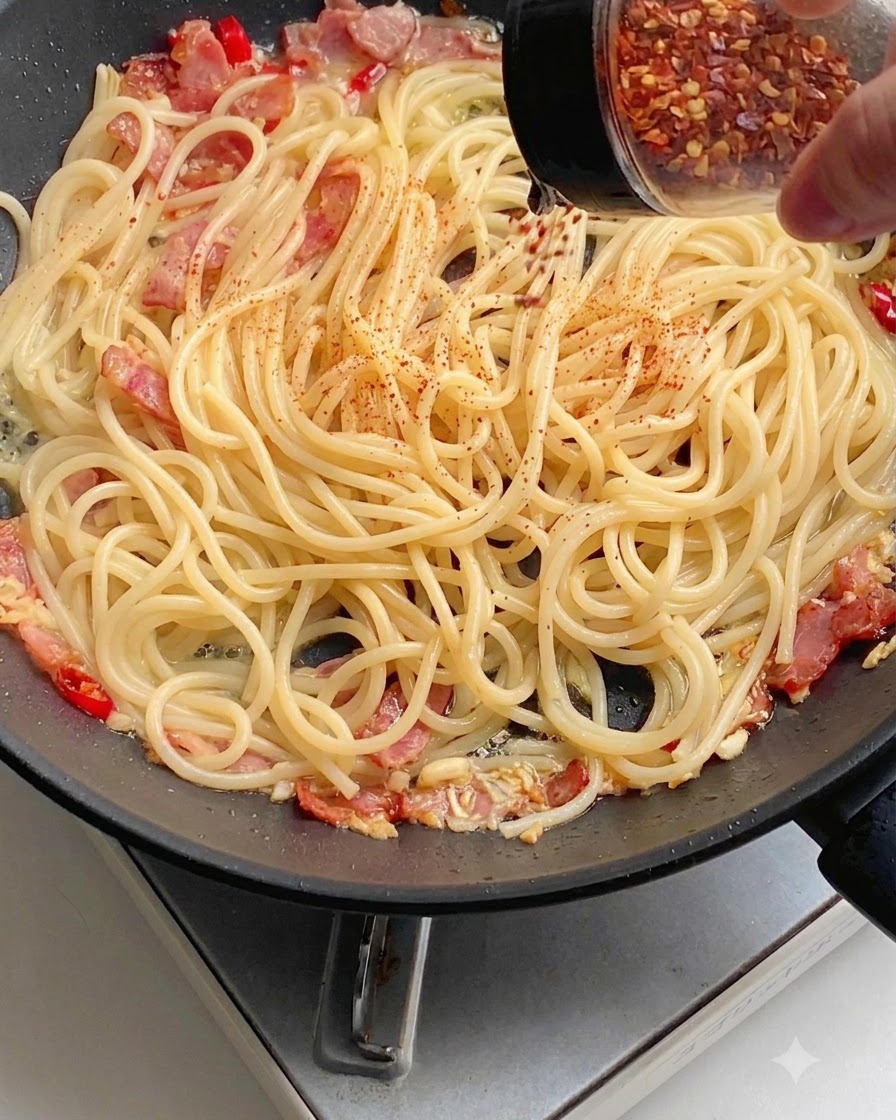 Du piment rouge en poudre saupoudré uniformément sur les spaghettis dans une poêle.