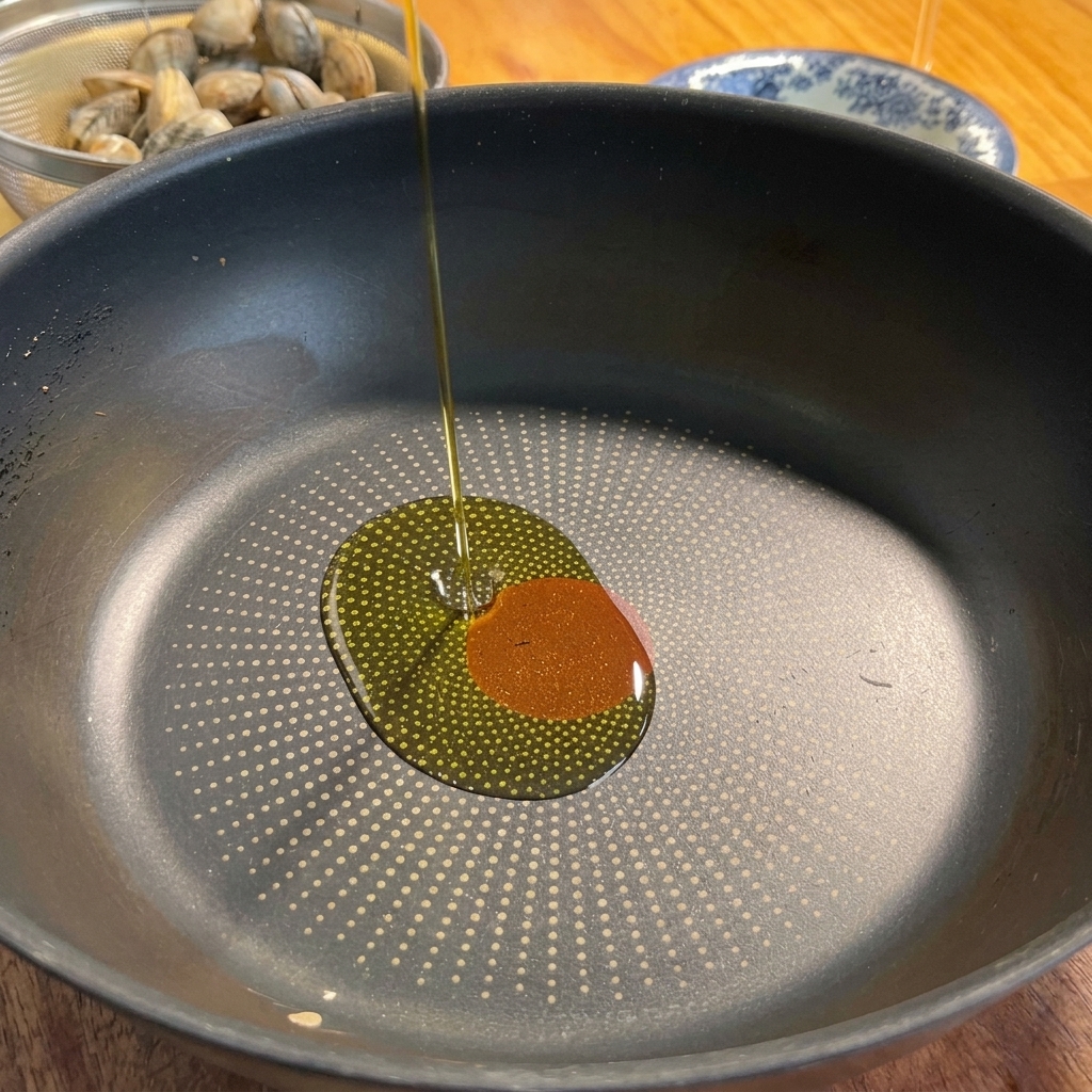 De lhuile dolive versée dans une poêle noire avec de lail et du piment.