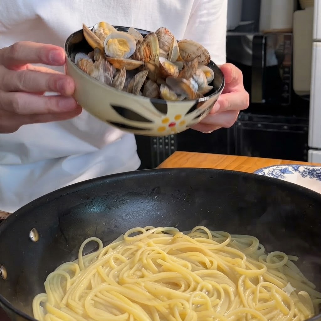 Une personne tenant un bol à motifs et versant des palourdes cuites dans une poêle remplie de spaghetti.
