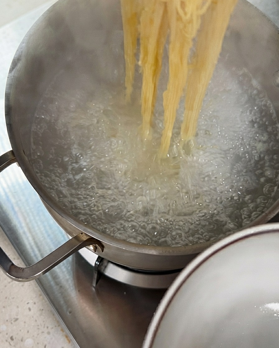 Pinces soulevant des brins de nouilles cuites hors dune casserole deau bouillante.